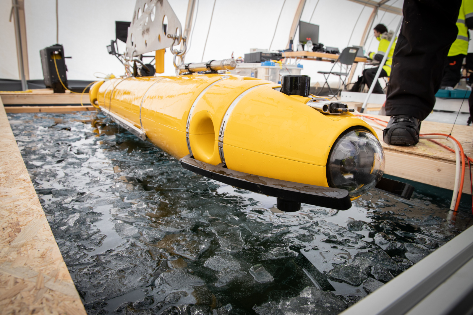 Ein gelbes Unterwasserfahrzeug wird in einem gefrorenen Gewässer ins Wasser gelassen, umgeben von Eis und einem Zeltaufbau.