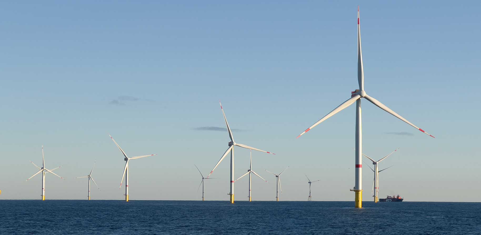 Several wind turbines stand in the water, with yellow bases and red-and-white striped blades under a clear sky.