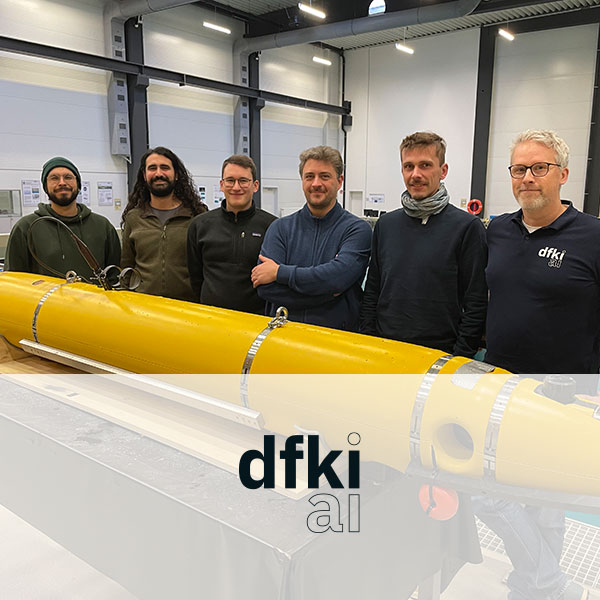 A group of six individuals stands in front of a long yellow device in a modern room, intended for research purposes.