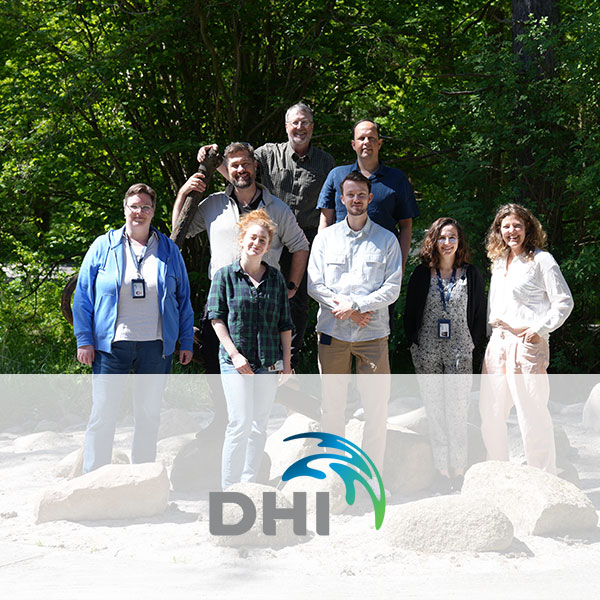 A group photo of eight people outdoors, surrounded by trees and rocks.