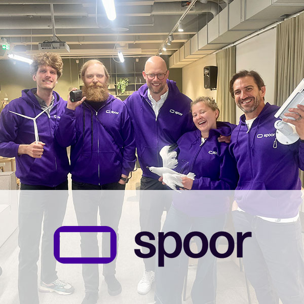 A group of five individuals in purple Spoor hoodies stands in a modern room. They are smiling and posing for the photo.