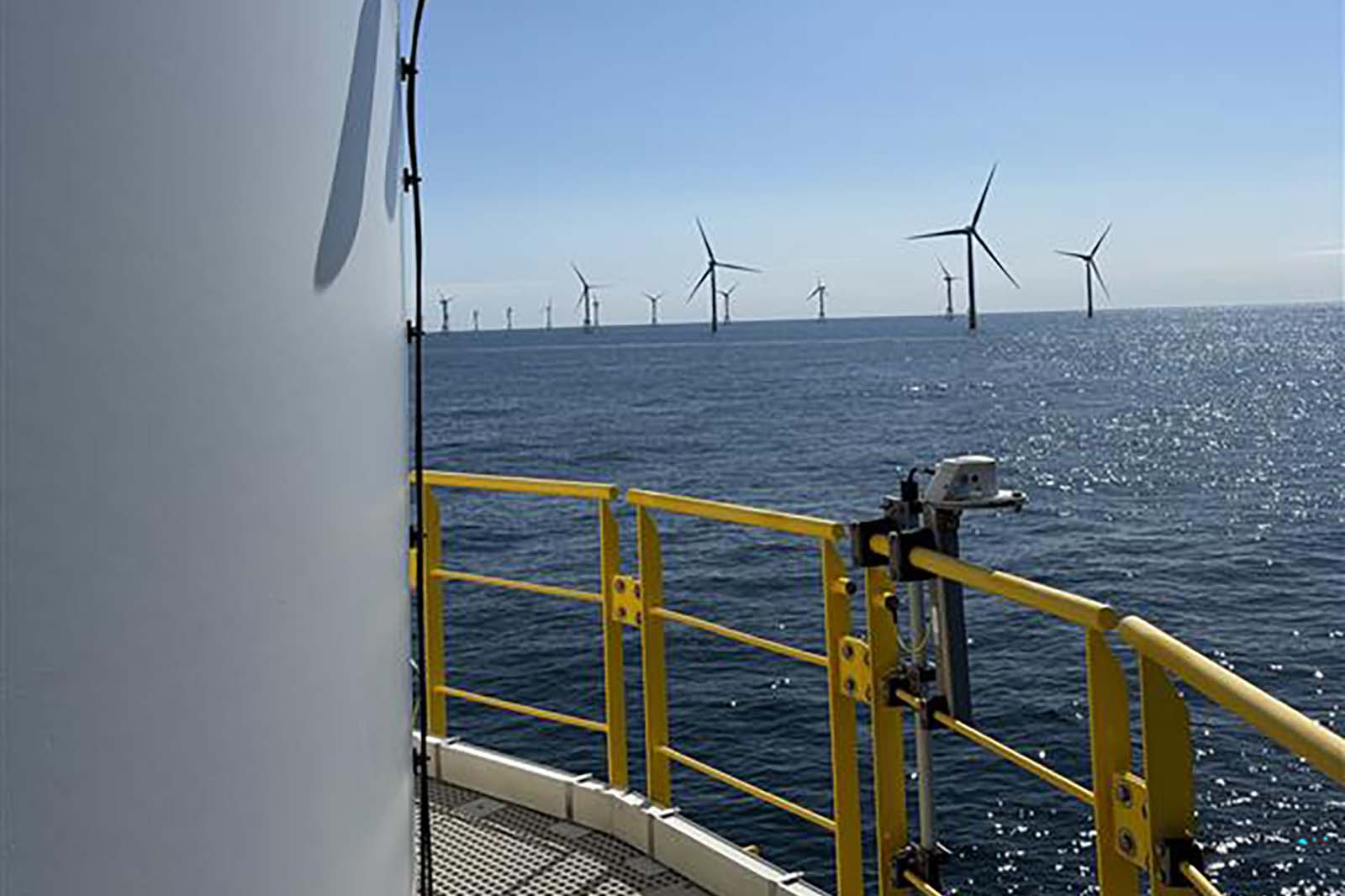 View from an offshore platform showing multiple wind turbines in the sea under a clear sky.