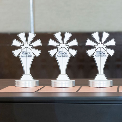Sechs elegante Auszeichnungen auf einem Tisch mit der Inschrift 'IMCA Awards 2025', in einer modernen Umgebung.